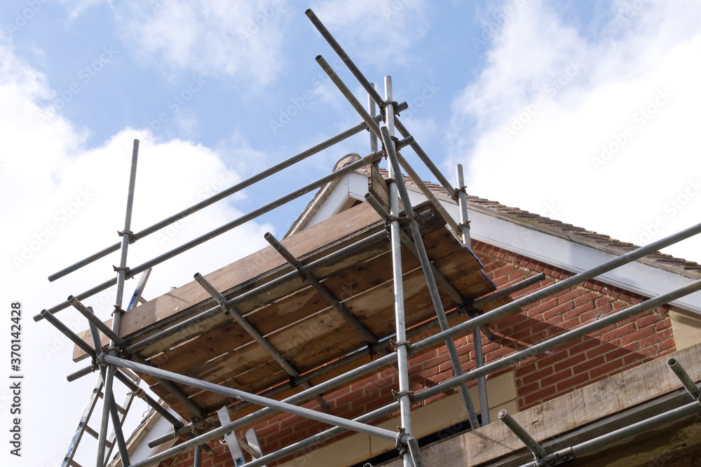 Modern house roof construction with scaffold pole platform. New build domestic building against blue sky with clouds Modern house roof construction with scaffold pole platform. New build domestic building against blue sky with clouds