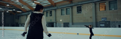 Young small girl professional figure skater parcticing jumps with her trainer on ice. Shot on RED cinema camera with 2x Anamorphic lens, 75 FPS Slow motion photo