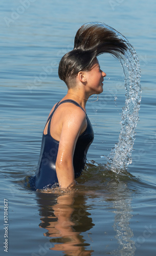the girl raises her head out of the water. young woman playing in sea. Brunette makes splashes with her hair.