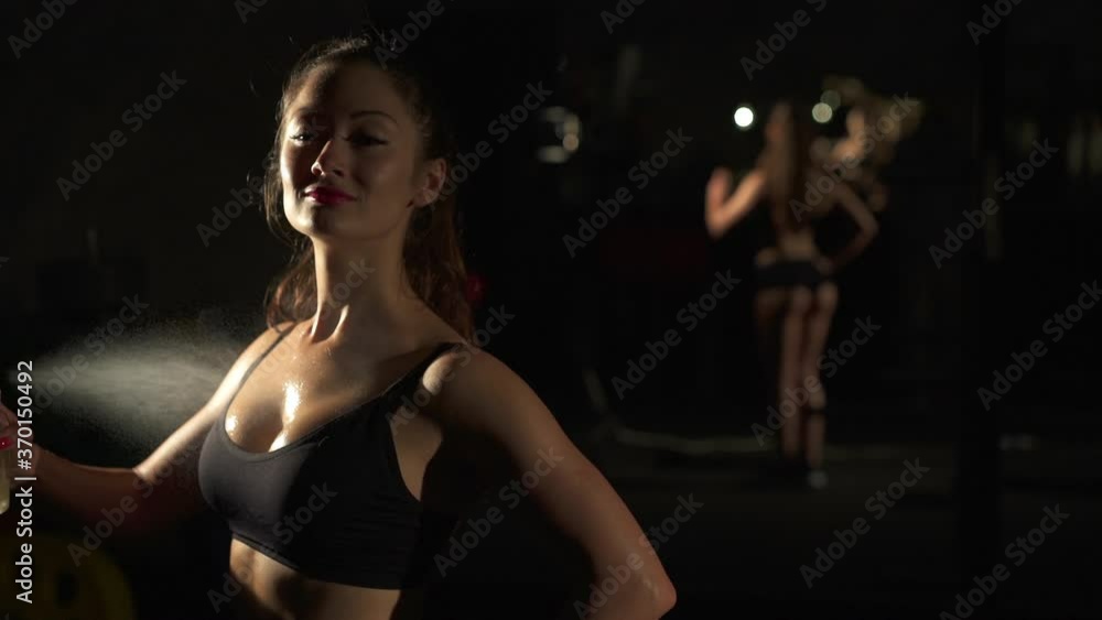 Athletic young sexy woman spraying body in front of mirror. Sporty gorgeous female smiling looking at herself in gym preparing for bodybuilding contest. Concept of sport, health, lifestyle. Athletic young sexy woman spraying body in front of mirror. Sporty gorgeous female smiling looking at herself in gym preparing for bodybuilding contest. Concept of sport, health, lifestyle.