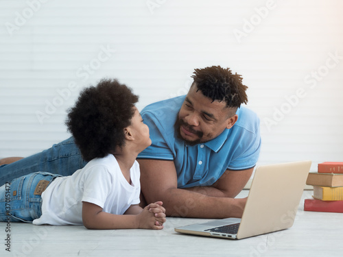 Black African father and son lying on floor looking at each other while using laptop. Bonding and Father's day concept.