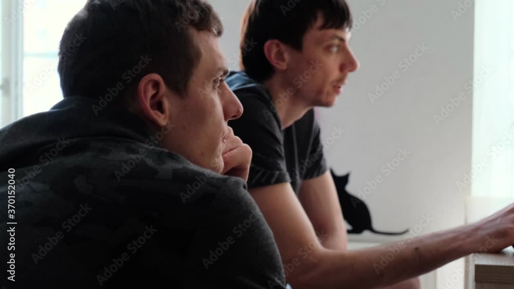 Two young men looking in the same direction and communicate sitting at home Two young men looking in the same direction and communicate sitting at home