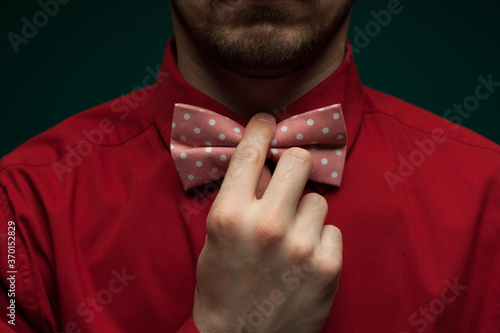 Fototapete Close-up of the hands of a young man in a red shirt correcting bow-tie against a green background