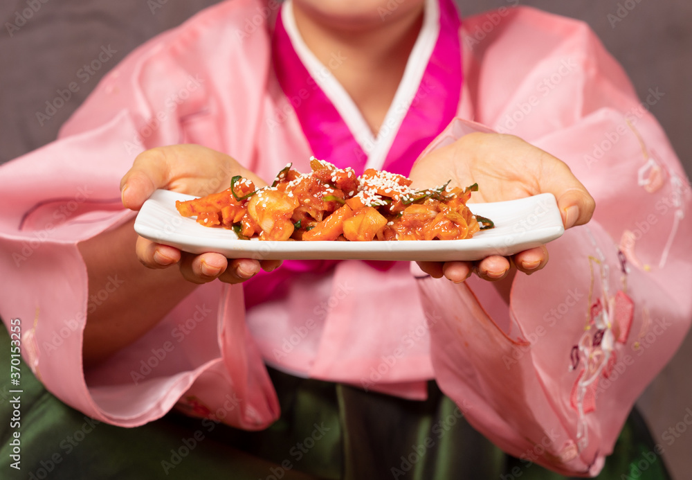 Close up, hand of Korean woman in traditional clothes, Hanbok, holding plate of colorful Kimchi.
