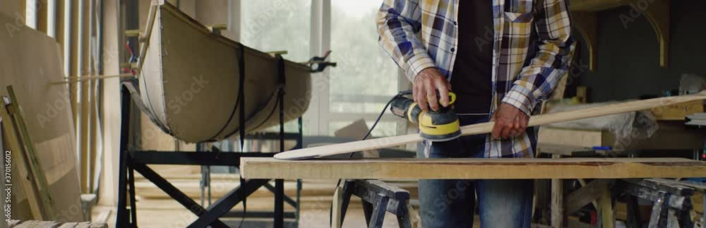 Mid 50s Caucasian male sanding a hand made canoe paddle in his workshop. Boat making hobby, small business owner Mid 50s Caucasian male sanding a hand made canoe paddle in his workshop. Boat making hobby, small business owner