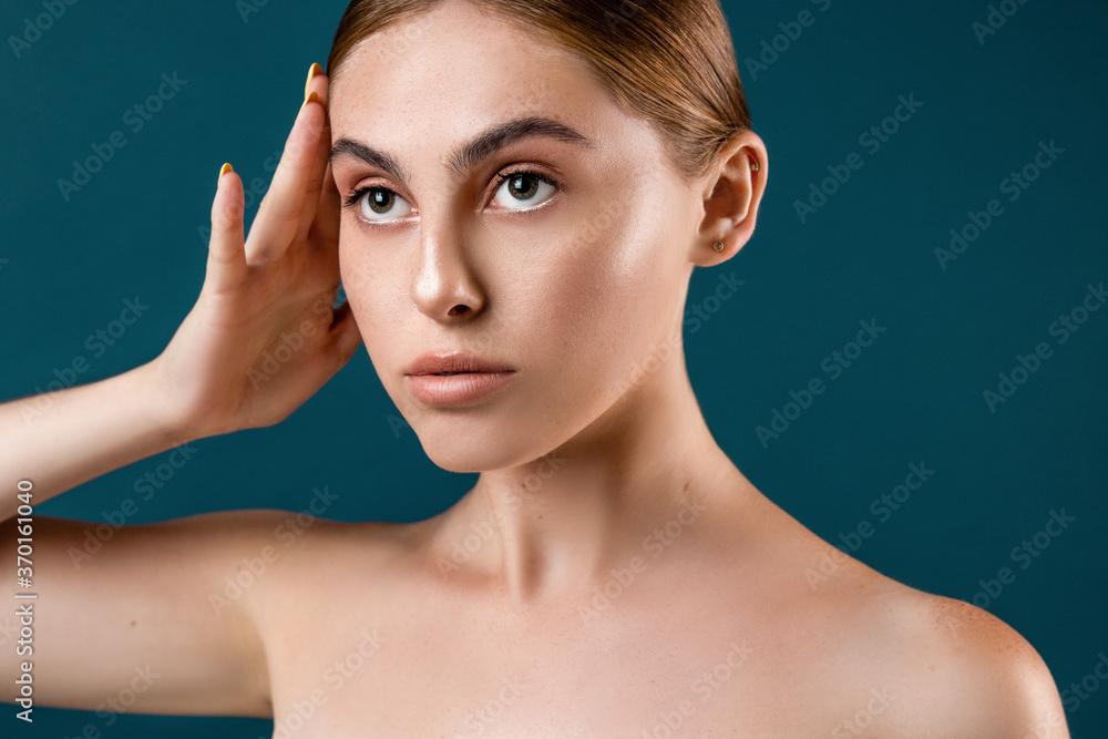 Beautiful young woman with clean perfect skin. Hand pose near head. Portrait of beauty model with natural nude make up and long eyelashes. Blue solid background. Beautiful young woman with clean perfect skin. Hand pose near head. Portrait of beauty model with natural nude make up and long eyelashes. Blue solid background.