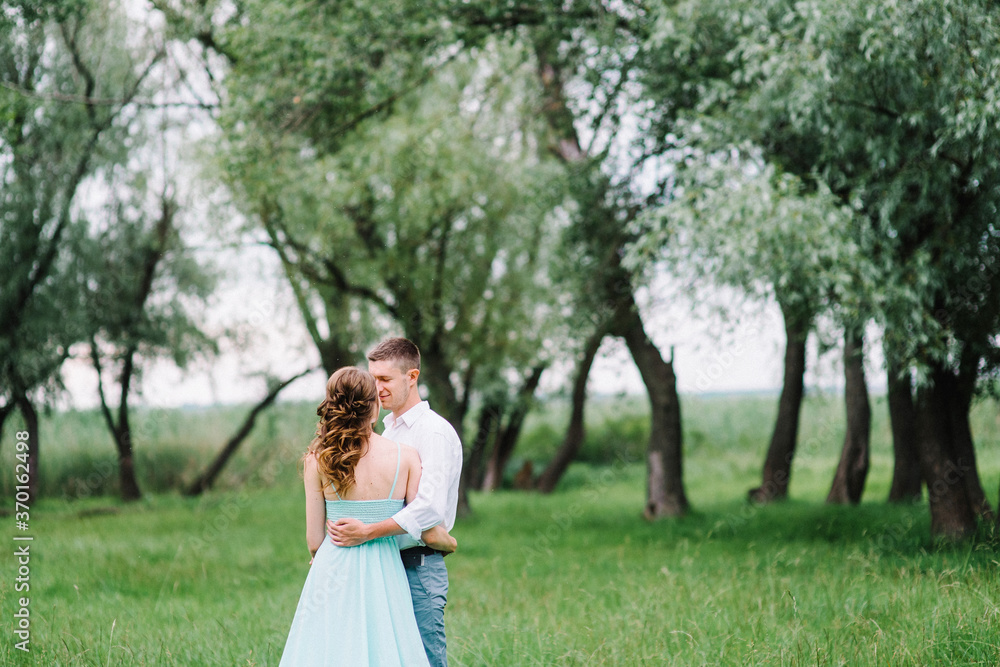 happy guy in a white shirt and a girl in a turquoise dress are walking in the forest park happy guy in a white shirt and a girl in a turquoise dress are walking in the forest park