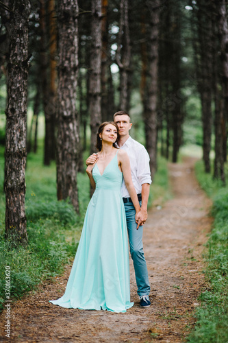 happy guy in a white shirt and a girl in a turquoise dress are walking in the forest park