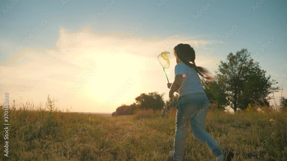 A happy, carefree child runs through a green field, enjoys nature, fresh air. A girl at sunset on a summer day holding a net, a child's toy for catching insects. A happy, carefree child runs through a green field, enjoys nature, fresh air. A girl at sunset on a summer day holding a net, a child's toy for catching insects.