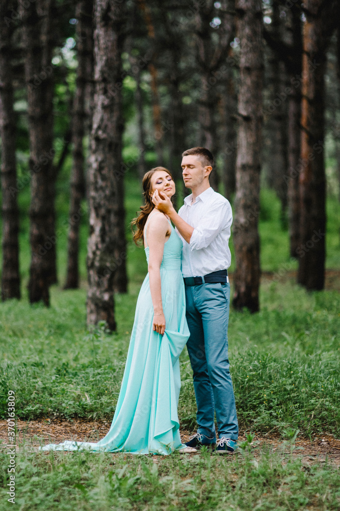 happy guy in a white shirt and a girl in a turquoise dress are walking in the forest park happy guy in a white shirt and a girl in a turquoise dress are walking in the forest park