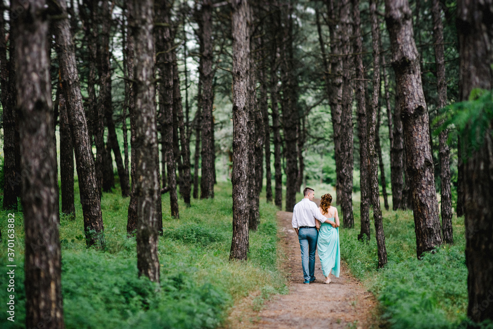 happy guy in a white shirt and a girl in a turquoise dress are walking in the forest park