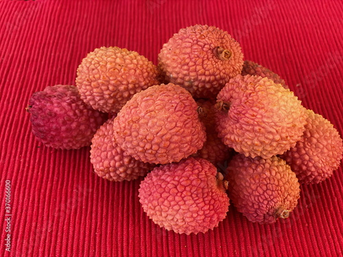 Lychee- small rounded fruit with sweet white scented flesh, a large central stone, and a thin rough skin- on red cloth napkin on table. Selective focus