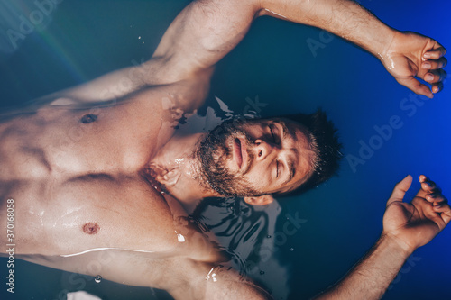 Foto Handsome beard man floating in tank filled with dense salt water used in meditation, therapy, and alternative medicine