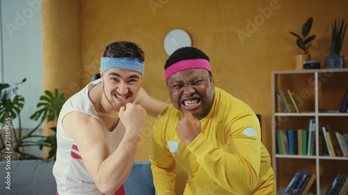 Fotografía Diverse crazy fitness freaks posing together, boasting of muscles kissing their biceps looking very confident recording funny sports vlog at home