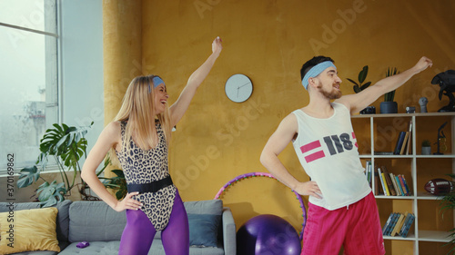 Funny caucasian retro couple doing warm-up aerobics exercises together. Female and male fitness lovers working out training at home in stylish vintage apartment. photo