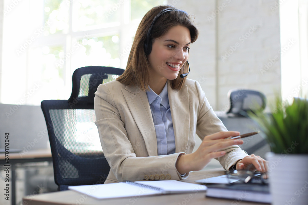 Beautiful smiling call center worker in headphones is working at modern office Beautiful smiling call center worker in headphones is working at modern office