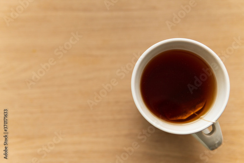 Black tea in white cup placed on wooden table. Focus on tea