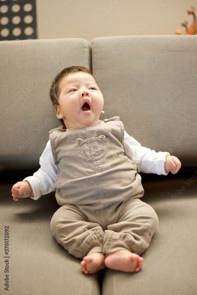 Cute baby boy in brown overall outfit sitting on sofa. Cute baby boy in brown overall outfit sitting on sofa.