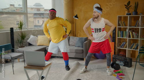 Weird funny multi-ethnic couple of retro athletes engaged in sports dancing into music stretching having fun at workout. Home isolation. Comical fitness team. photo