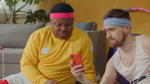 Comical sports couple of friends using smartphone after training, screwing up faces in big disgust watching nasty content on the internet. Expressions. Grimacing.