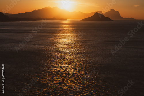 Beautiful yellow sunset over the sea and behind mountains reflecting on the sea. Sunrise over the ocean with golden sun rising from behind the mountain.