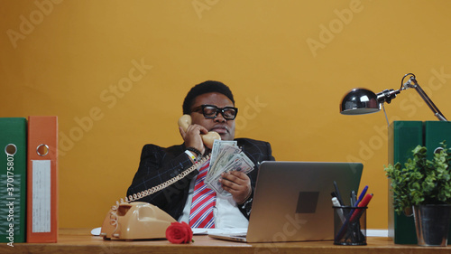 Emotional black business guy talking with partner on telephone call holding bunch of money arguing in conflict. Office space. Business people.