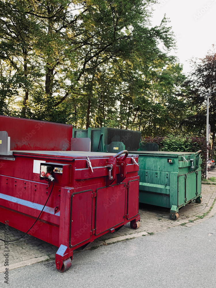 on an industrial site a green waste compactor and a red waste compactor stand side by side on an industrial site a green waste compactor and a red waste compactor stand side by side