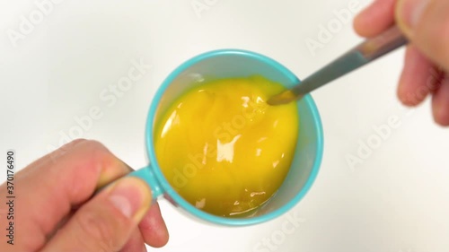 Mixing a fork of yolks and albumens of chicken eggs in a blue mug on a white background. Slow motion close-up. Preparing an amlet for a delicious and healthy breakfast photo