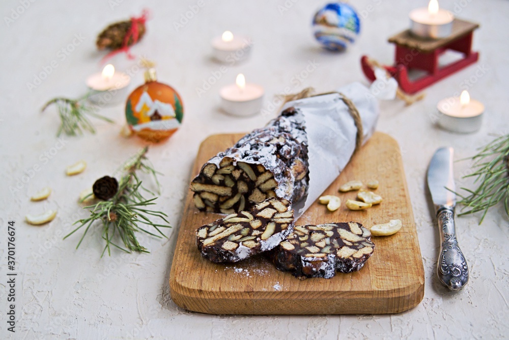 Dessert, chocolate salami with cookies and cashews in the New Year and Christmas style on a wooden board on a light concrete background. Dessert, chocolate salami with cookies and cashews in the New Year and Christmas style on a wooden board on a light concrete background.