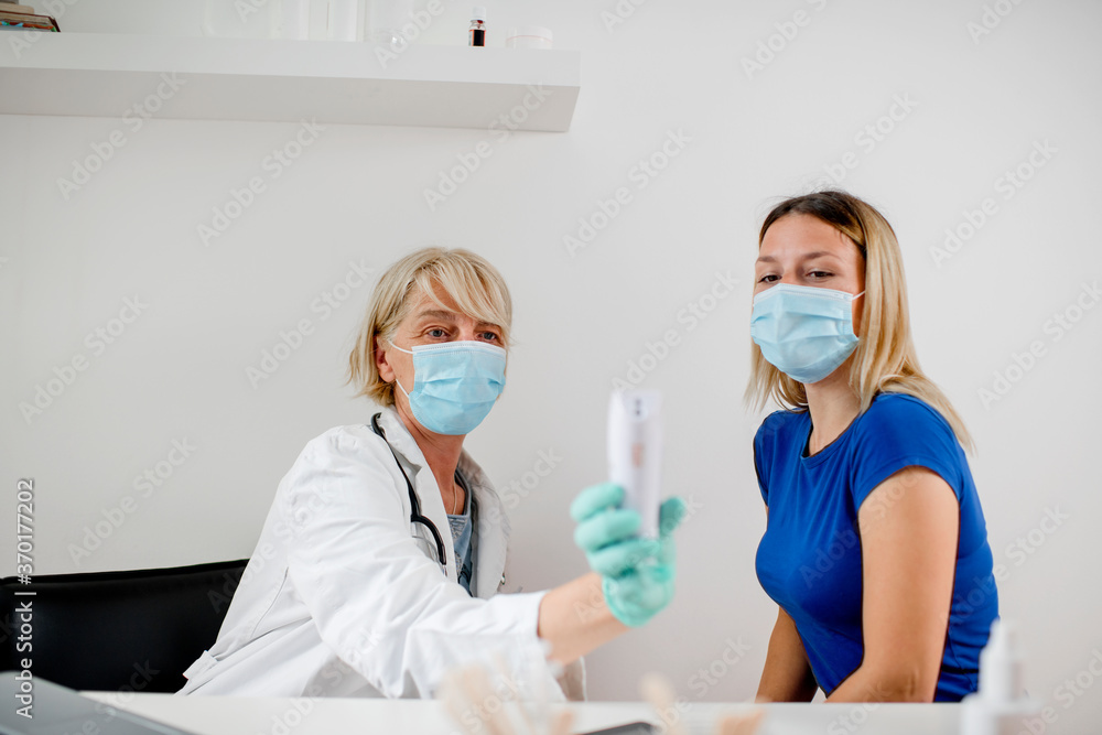 Female doctor doing medical exam to a young woman. They are wearing a protective face mask. Female doctor doing medical exam to a young woman. They are wearing a protective face mask.