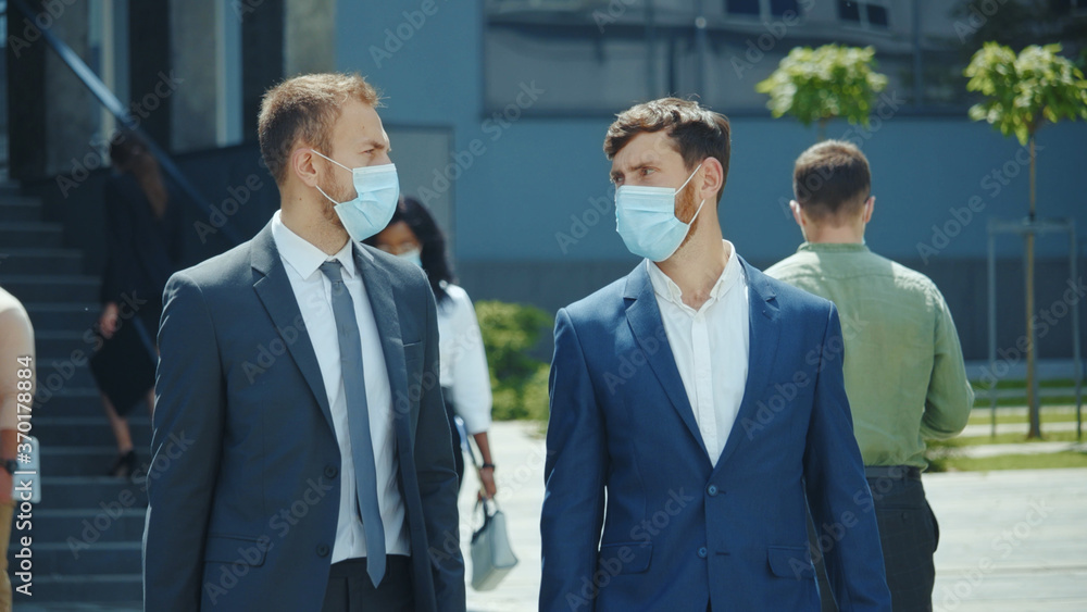 Two business men in protective mask walk outside office building. Corporate people having break at workspace. Work after lockdown. Employment. Business people. Two business men in protective mask walk outside office building. Corporate people having break at workspace. Work after lockdown. Employment. Business people.