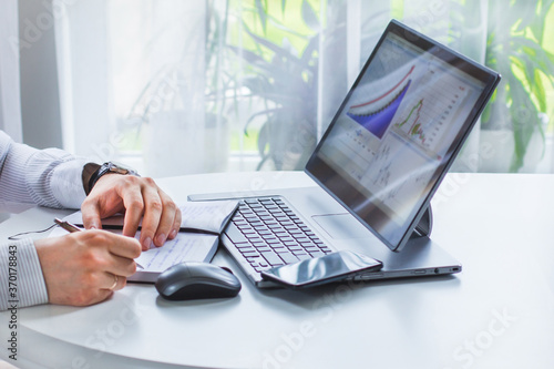 An image of the hands of a man who is sitting at a table, holding a phone in one hand and a ballpoint pen in the other, writing in a notebook, next to a computer mouse photo
