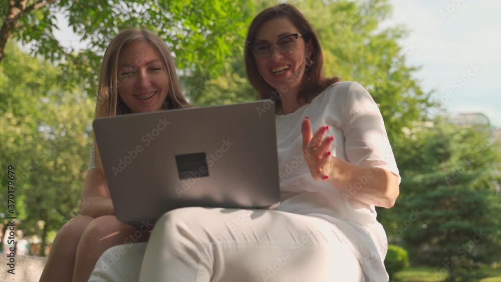 Young woman helping her old retired mother on a laptop sitting in a park. Concept of Age Inclusivity Young woman helping her old retired mother on a laptop sitting in a park. Concept of Age Inclusivity