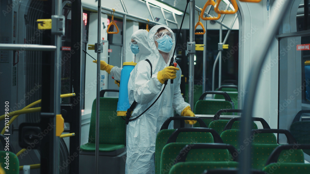 Disinfection team of workers cleaning tram after working day. Janitor in white bodysuit face mask disinfecting public transport with professional equipment. Disinfection team of workers cleaning tram after working day. Janitor in white bodysuit face mask disinfecting public transport with professional equipment.