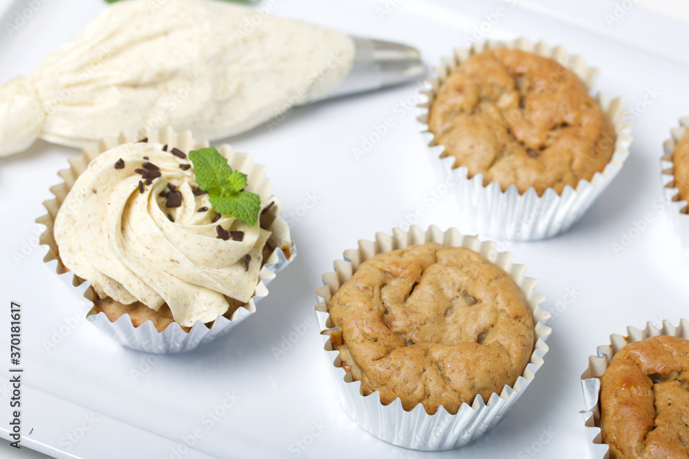 Banana cupcake. With butter cream and banana jam. Decorated with mint leaves and chocolate sprinkles. Next to them are cupcakes without cream and a pastry bag with cream. Banana cupcake. With butter cream and banana jam. Decorated with mint leaves and chocolate sprinkles. Next to them are cupcakes without cream and a pastry bag with cream.