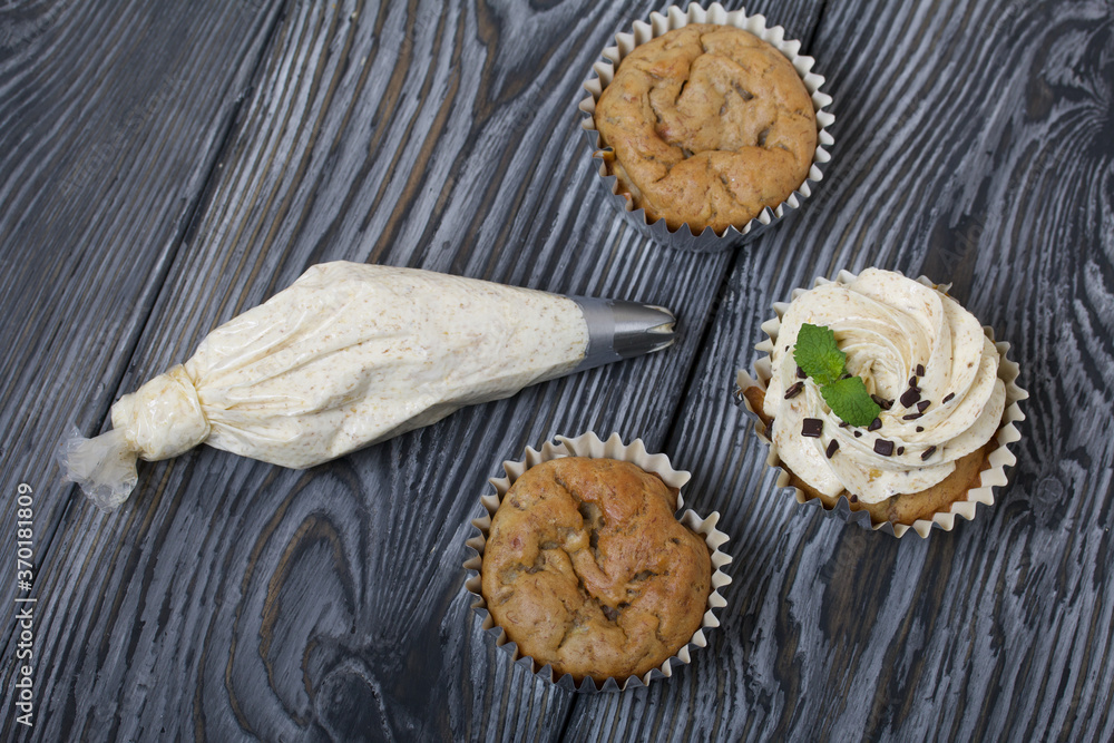 Banana cupcake. With butter cream and banana jam. Decorated with mint leaves and chocolate sprinkles. Next to them are cupcakes without cream and a pastry bag with cream. Banana cupcake. With butter cream and banana jam. Decorated with mint leaves and chocolate sprinkles. Next to them are cupcakes without cream and a pastry bag with cream.