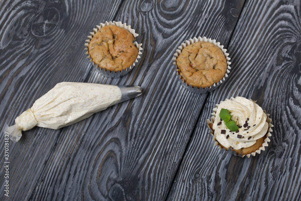 Banana cupcake. With butter cream and banana jam. Decorated with mint leaves and chocolate sprinkles. Next to them are cupcakes without cream and a pastry bag with cream. Banana cupcake. With butter cream and banana jam. Decorated with mint leaves and chocolate sprinkles. Next to them are cupcakes without cream and a pastry bag with cream.