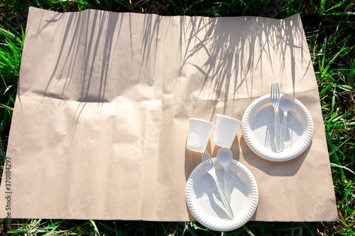 two sets of disposable biodegradable tableware for an outdoor picnic. cornstarch forks, spoons, plates and glasses. eco friendly concept. grass shadow. place for text.