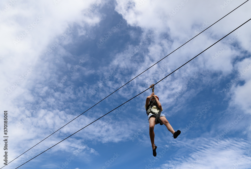 Closeup of a boy gliding on extreme trolley zip-line in adventure park with cloudy blue sky background. 