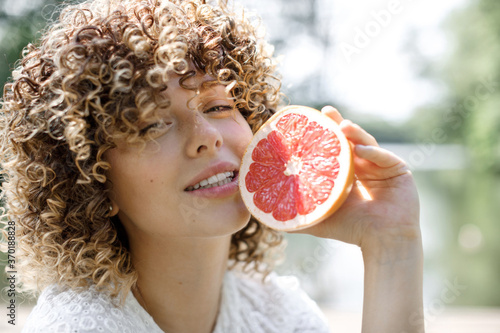 Portrait of a happy healthy woman with curly hair and freckles who holds a grapefruit near her face. Healthy food, health and personal care concept photo