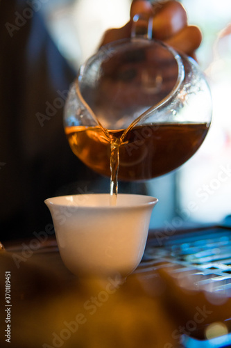 Traditional Chinese Tea Ceremony. Black or Red Tea pouring into White pial cup on dark Table background