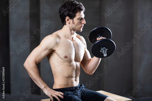 Determined attractive young man naked torso exercising with dumbbell.
