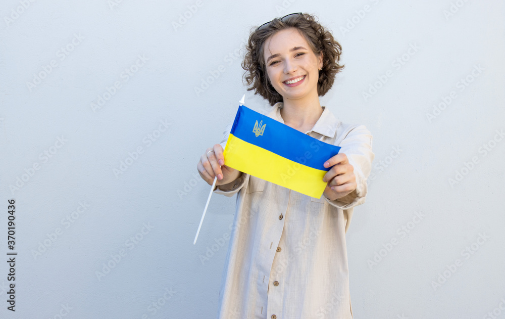 Young beautiful woman with curly hair with the flag of Ukraine on a gray wall background. Young beautiful woman with curly hair with the flag of Ukraine on a gray wall background.