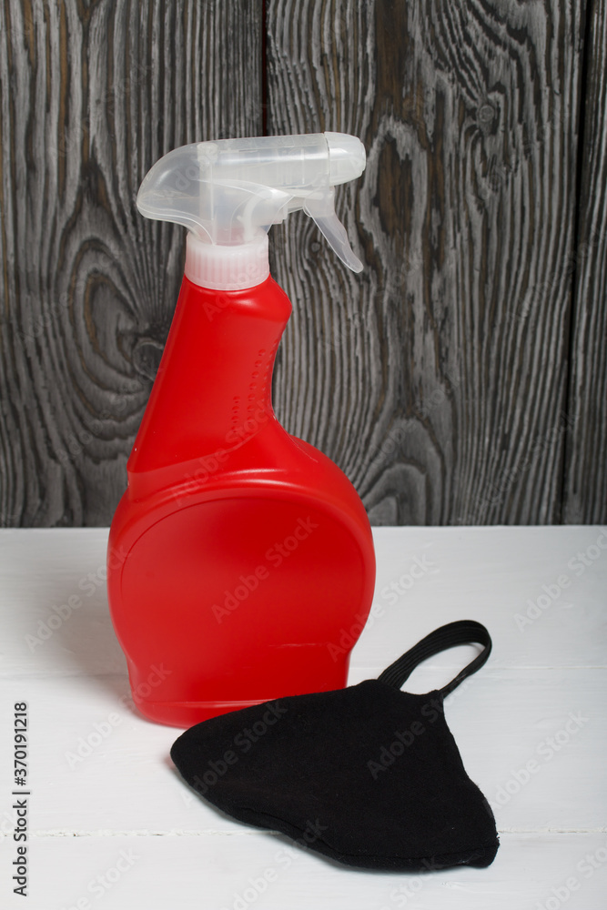 Red plastic bottle with spray. Cleaning spray. Face mask to protect against the virus. The mask is black.