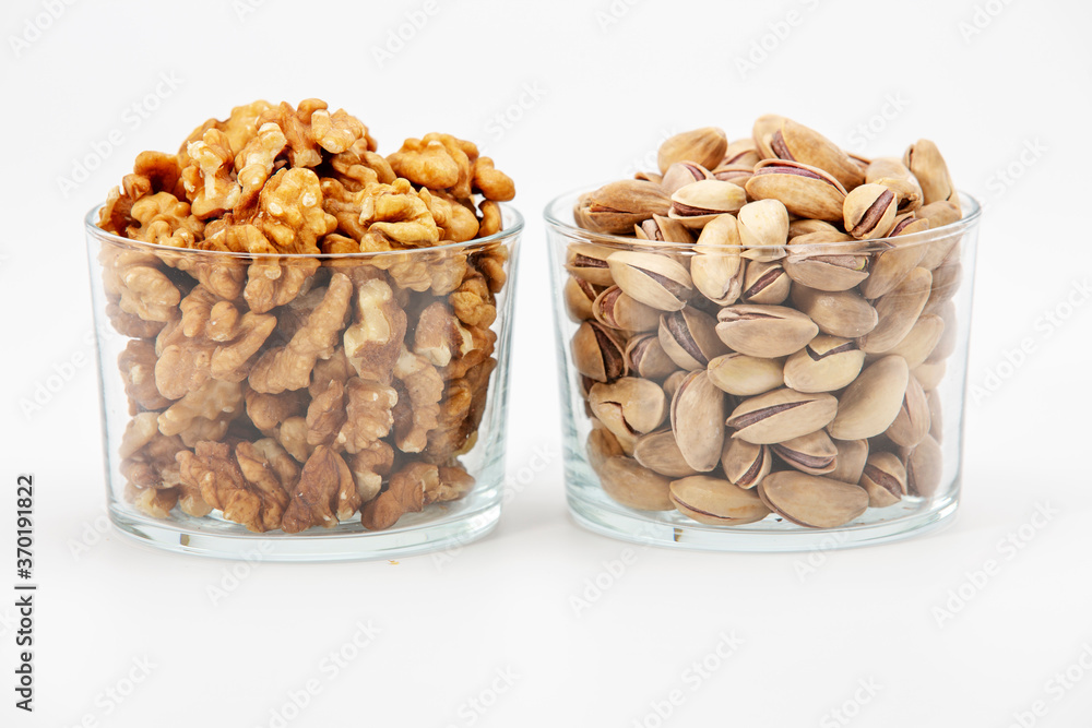 Pile of salted pistachios and walnuts in glass bowl on white background. Pile of salted pistachios and walnuts in glass bowl on white background.