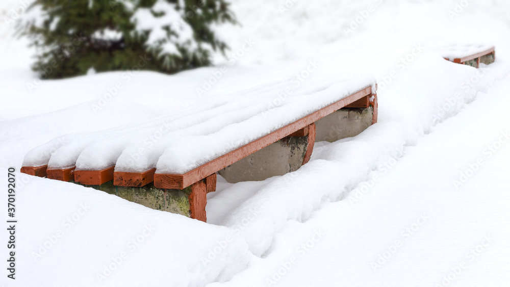 Bench in a park covered completely by snow after heavy snowfall Bench in a park covered completely by snow after heavy snowfall