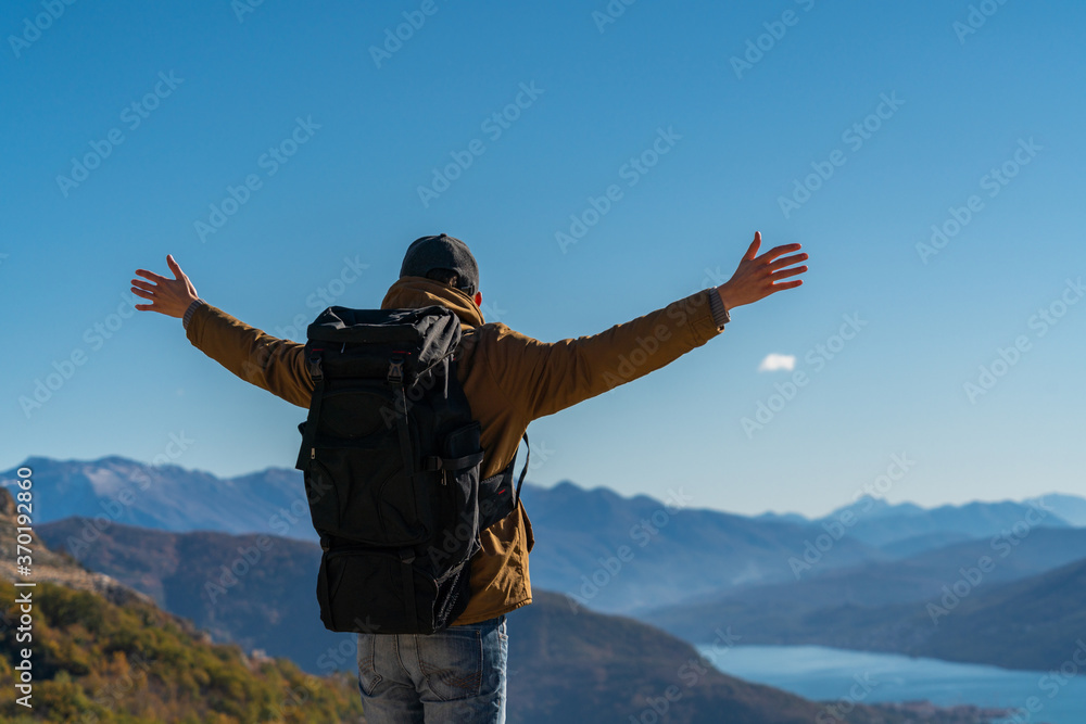 A traveler with a backpack stands on the top of the mountain and holds his hands to the sides A traveler with a backpack stands on the top of the mountain and holds his hands to the sides