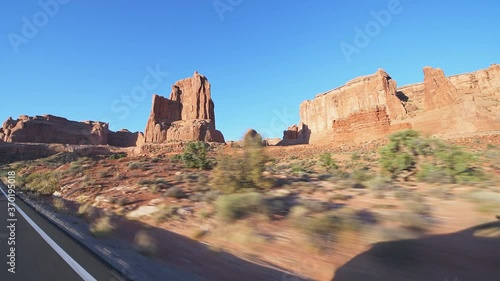 Pov point of view panning driving car side view shot on arches scenic drive at Arches National Park near Moab, Utah at sunrise with canyons rock formations and vehicle shadow on road trip