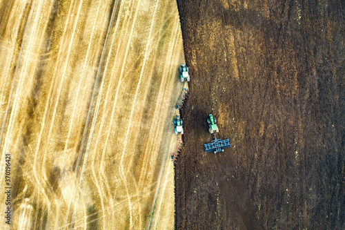 Aerial view of a tractor plowing black agriculture farm field after harvesting in late autumn.