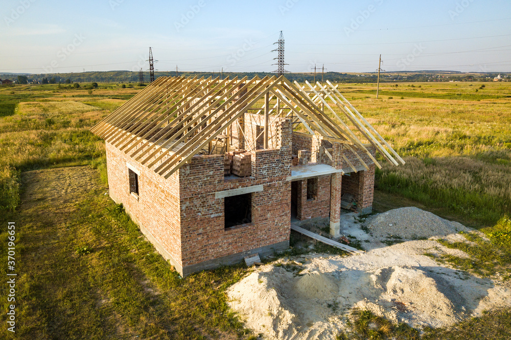 Unfinished brick house with wooden roof structure under construction.